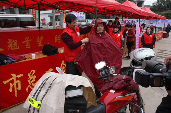 梧州市總工會的黨員義工們在市東出口春運服務站助力“摩托大軍”平安返鄉(xiāng)，幫助他們檢查車輛和行李，穿上雨衣。--黃賀峰攝.j